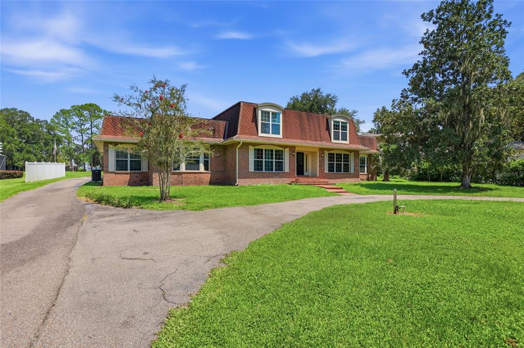 A brick house with a mansard roof and a circular driveway sits on a grassy lawn — 6319 SW 37TH WAY, GAINESVILLE, FL