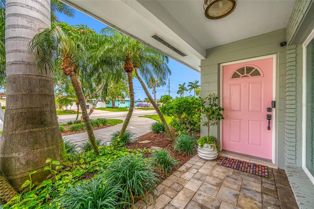 A covered front porch features a pink door, stone pavers, and tropical landscaping — 560 79TH STREET S, ST PETERSBURG, FL