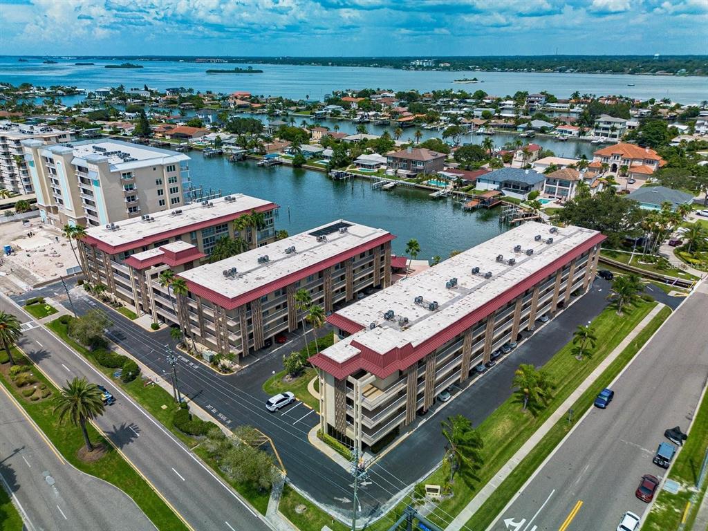 An aerial view shows three multi-story apartment buildings situated near a canal and bay — 105 ISLAND WAY UNIT 138, CLEARWATER, FL