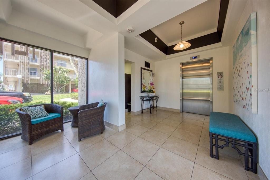 A lobby area features tile floors, a stainless steel elevator, and seating near large windows — 105 ISLAND WAY UNIT 138, CLEARWATER, FL