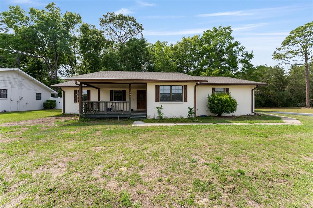 A single-story house with a covered front porch, brown shutters, and a large grassy yard — 11300 SE 74TH AVENUE, BELLEVIEW, FL