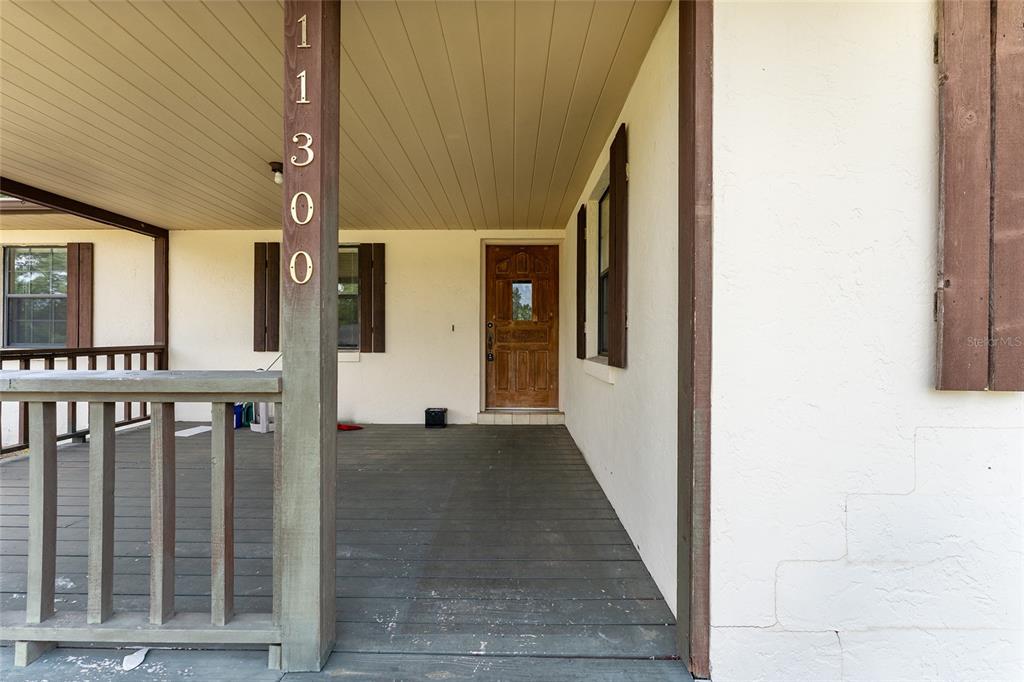 A covered front porch features a wooden deck, a railing, and a wooden front door — 11300 SE 74TH AVENUE, BELLEVIEW, FL