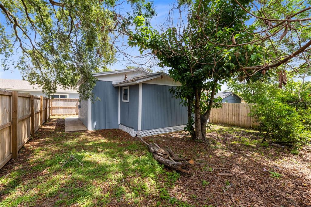 A blue-sided detached structure sits in a backyard with a wooden fence and trees — 3432 HARRY STREET, APOPKA, FL