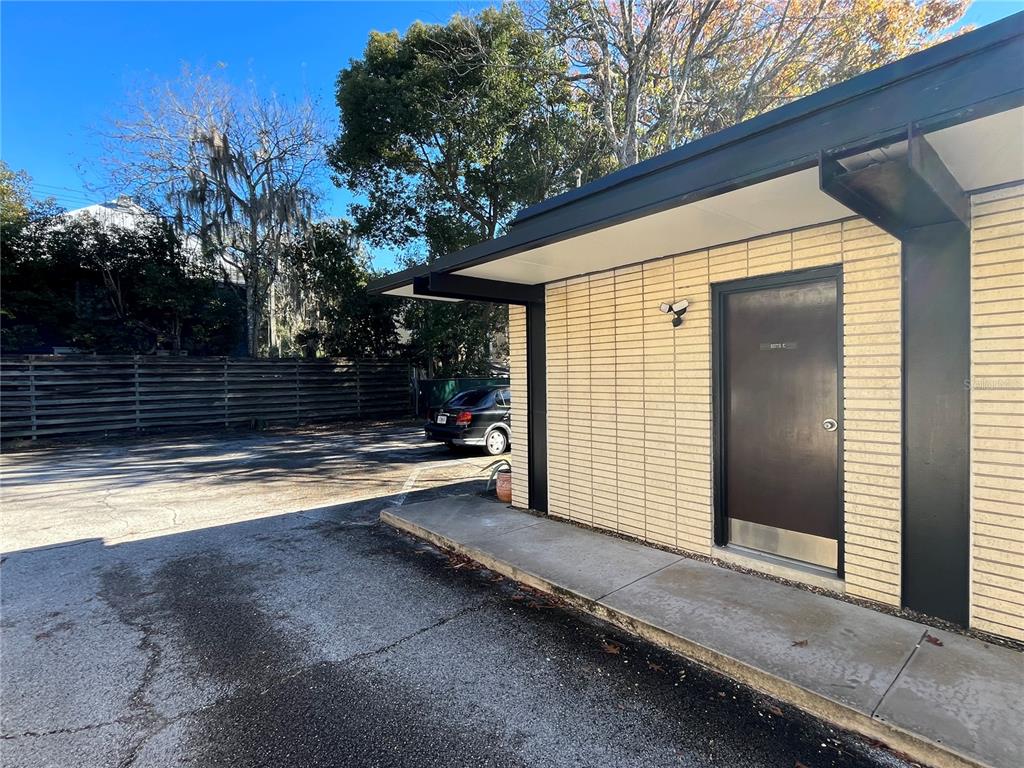 A dark door is set into a tan brick wall under a flat roof overhang — 519 NE 1ST STREET, GAINESVILLE, FL