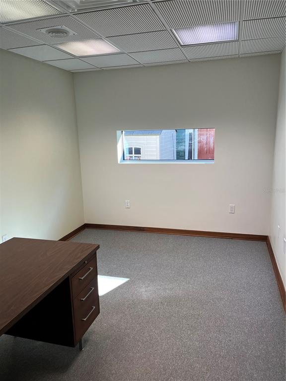 An office space features gray carpeting, white walls, a desk, and a horizontal rectangular window — 519 NE 1ST STREET, GAINESVILLE, FL