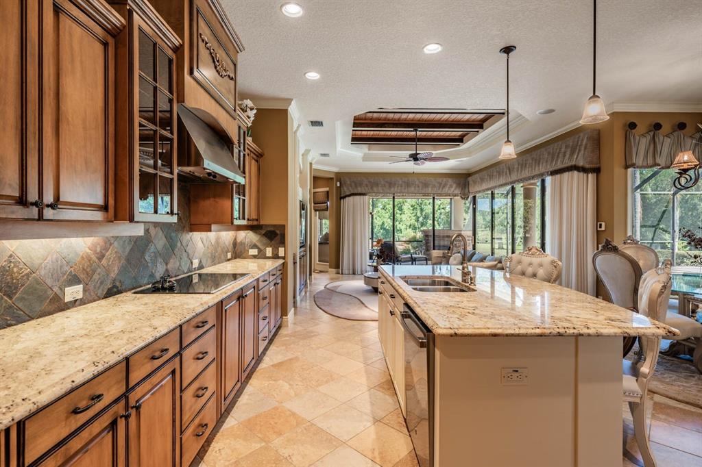 A kitchen with wood cabinets, granite countertops, and a central island overlooks a living area — 13327 CARNOUSTIE CIRCLE, DADE CITY, FL