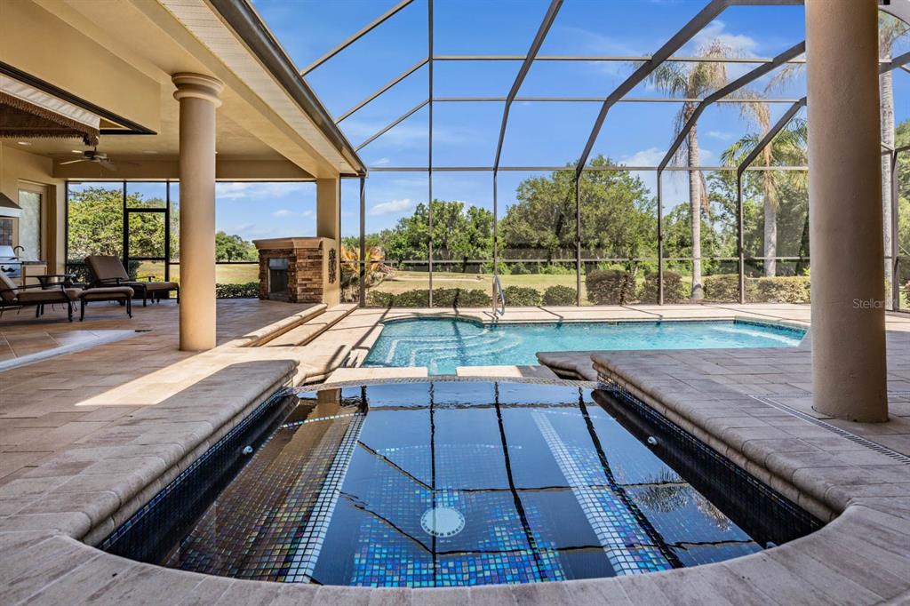 A screened-in patio features a tiled hot tub, a swimming pool, and an outdoor fireplace — 13327 CARNOUSTIE CIRCLE, DADE CITY, FL