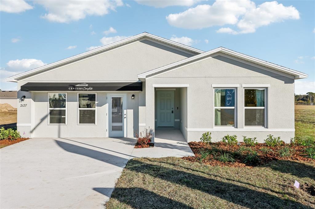 A single-story house with a light-colored stucco exterior, a concrete driveway, and a covered entryway — 910 AVERY STREET S, LEHIGH ACRES, FL