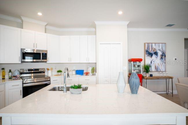 A bright kitchen features white cabinets, a large quartz island, and stainless steel appliances — 25462 CALUSA DRIVE, PUNTA GORDA, FL