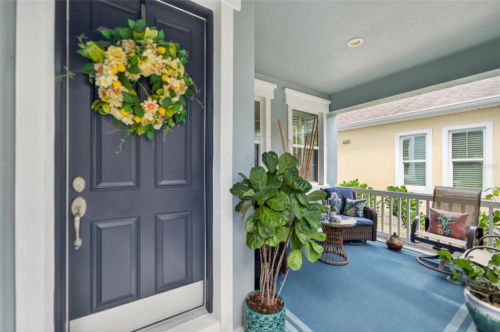 A covered front porch features a blue door with a wreath and outdoor seating — 623 WINTERSIDE DRIVE, APOLLO BEACH, FL