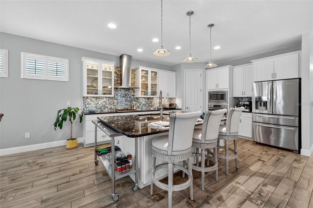 A modern kitchen features white cabinetry, a granite-topped island with seating, and wood-look tile flooring — 623 WINTERSIDE DRIVE, APOLLO BEACH, FL