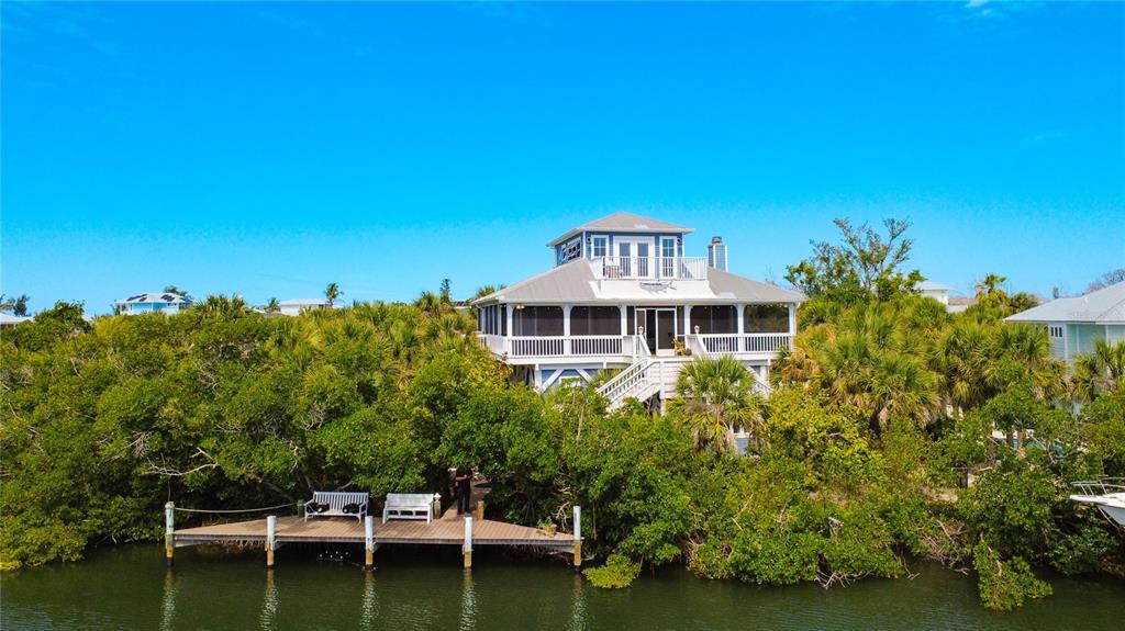 An elevated house with a screened porch and a private dock sits among lush trees — 39 BAYSHORE CIRCLE, PLACIDA, FL