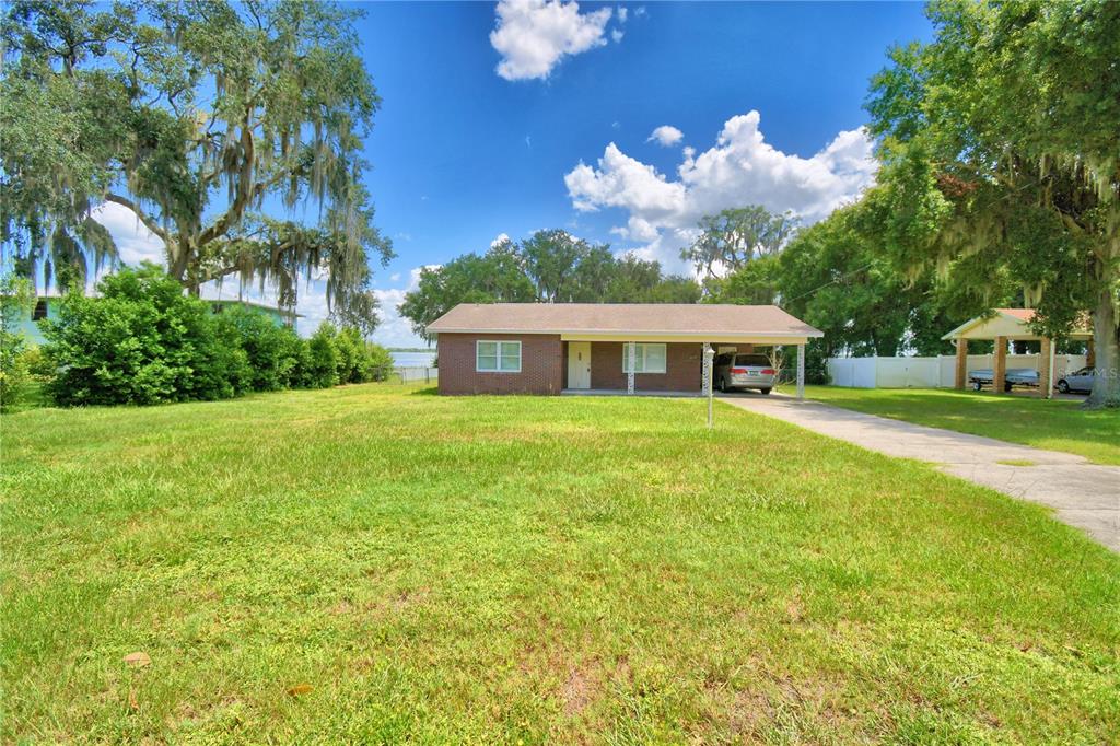 A single-story brick house with a carport sits on a large grassy lot — 214 N LAKE REEDY BOULEVARD, FROSTPROOF, FL