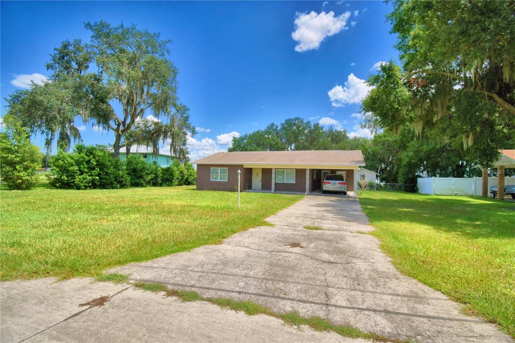 A single-story brick house with a carport and a concrete driveway sits on a lawn — 214 N LAKE REEDY BOULEVARD, FROSTPROOF, FL