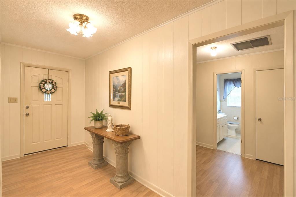 An entryway features light wood-look flooring, paneled walls, a console table, and a doorway to a bathroom — 214 N LAKE REEDY BOULEVARD, FROSTPROOF, FL