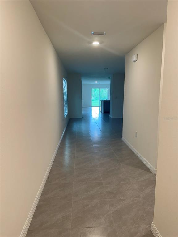 A long hallway with light-colored tile flooring leads toward a bright room with sliding doors — 1663 HAZY SEA DRIVE, PLANT CITY, FL