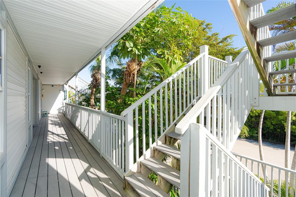 An outdoor wooden walkway with white railings leads to a staircase under a covered porch — 7450 PALM ISLAND DRIVE UNIT 3411, PLACIDA, FL