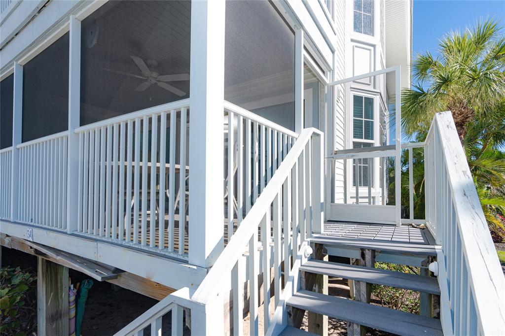 An elevated screened-in porch with white railings and stairs leading to a wooden deck — 7450 PALM ISLAND DRIVE UNIT 3411, PLACIDA, FL