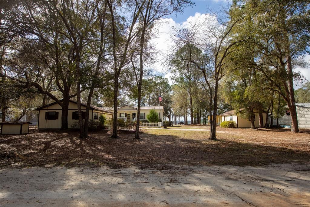 A view of a light-colored house with a white fence surrounded by many trees — 5711 CARIBBEAN CIRCLE, KEYSTONE HEIGHTS, FL