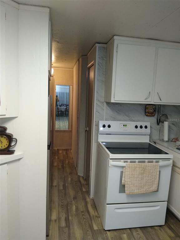 A kitchen features white cabinets, a white electric stove, and wood-look flooring in a hallway — 8488 SE 126TH PLACE, BELLEVIEW, FL