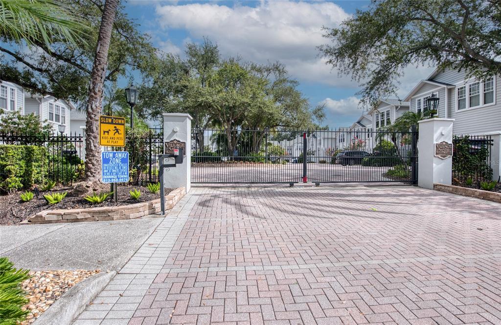 A gated entrance with brick pavers leads to a residential complex with light-colored siding — 2311 W MORRISON AVENUE UNIT 26, TAMPA, FL