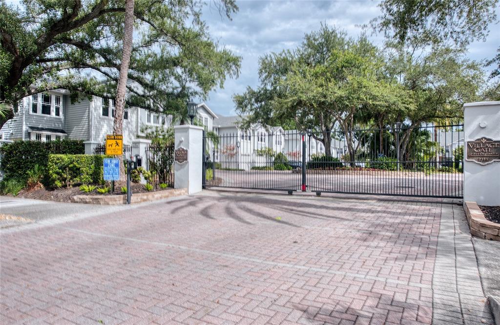 A gated entrance with a brick driveway leads to a residential complex with light-colored buildings — 2311 W MORRISON AVENUE UNIT 26, TAMPA, FL