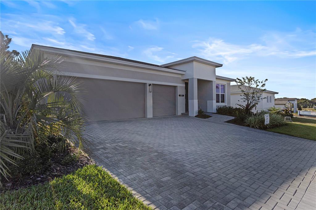 A modern single-story house features a two-car garage and a paved driveway under a blue sky — 1727 POINT GRACE ROAD, TAVARES, FL