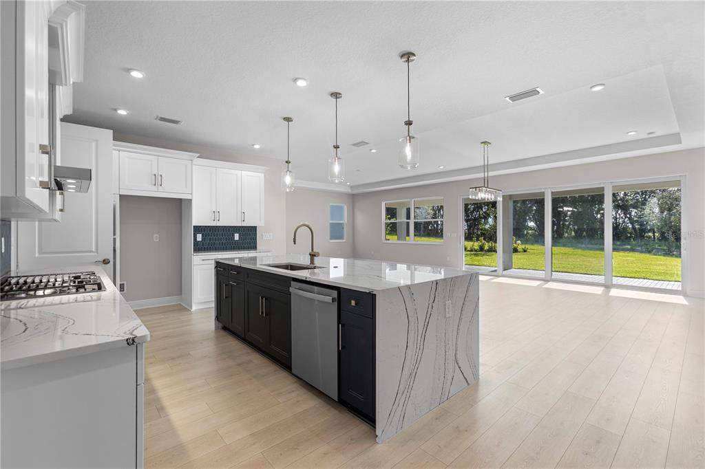 A modern kitchen features white cabinets, a dark island with a waterfall countertop, and large windows — 1727 POINT GRACE ROAD, TAVARES, FL