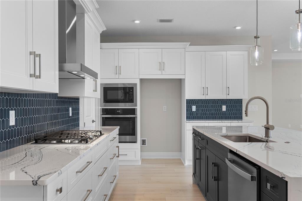 A modern kitchen features white cabinets, a dark island, marble countertops, and blue tile backsplashes — 1727 POINT GRACE ROAD, TAVARES, FL