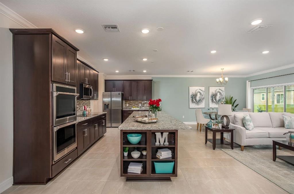 A kitchen with dark wood cabinets and a granite island opens to a living area — 17219 NW 173RD DRIVE, ALACHUA, FL
