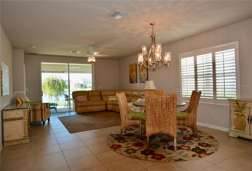 An open-concept living and dining area features tile floors, a chandelier, and sliding glass doors — 25161 E LENOX CIRCLE, PUNTA GORDA, FL