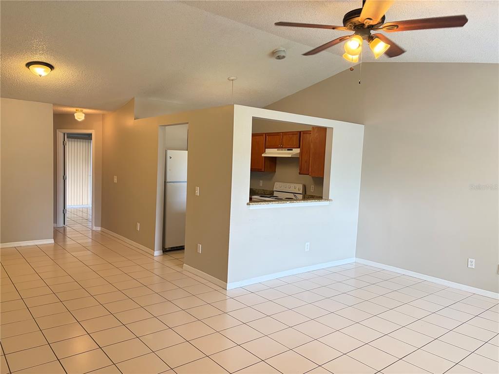 A living room with tiled floors and a ceiling fan opens to a kitchen pass-through — 1224 ROMA COURT, ORLANDO, FL