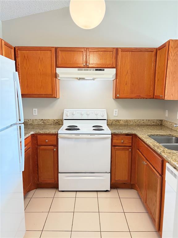 A kitchen features oak cabinets, granite countertops, white appliances, and light-colored floor tiles — 1224 ROMA COURT, ORLANDO, FL