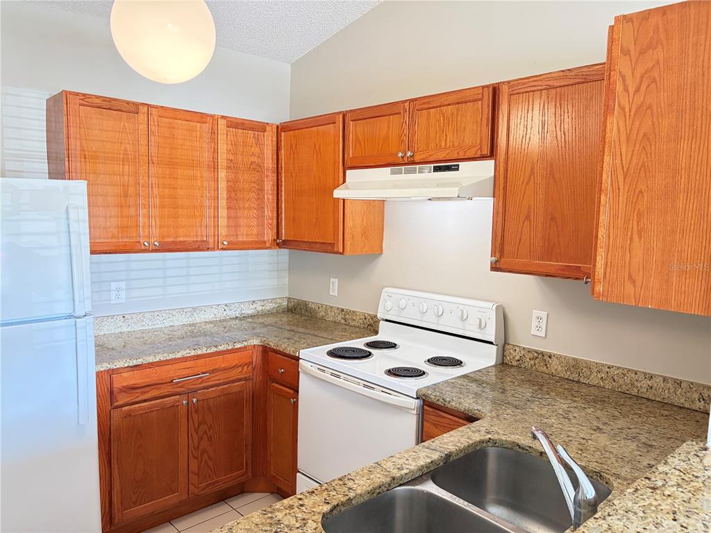 A kitchen features oak cabinets, granite countertops, a white stove, and a stainless steel sink — 1224 ROMA COURT, ORLANDO, FL