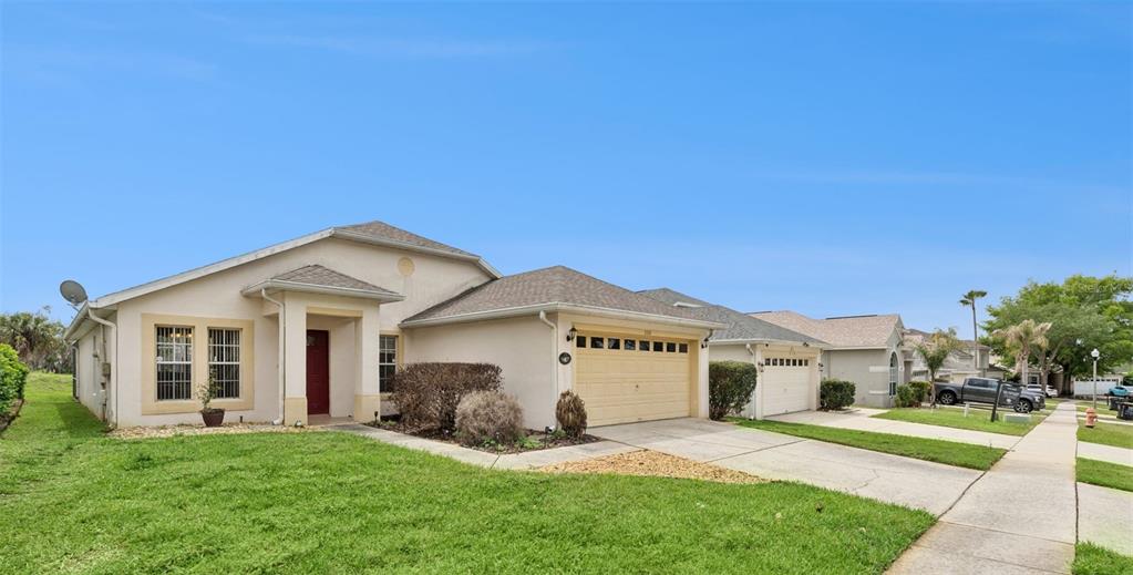 A single-story suburban house with a tan stucco exterior, a two-car garage, and a lawn — 228 TROON CIRCLE, DAVENPORT, FL