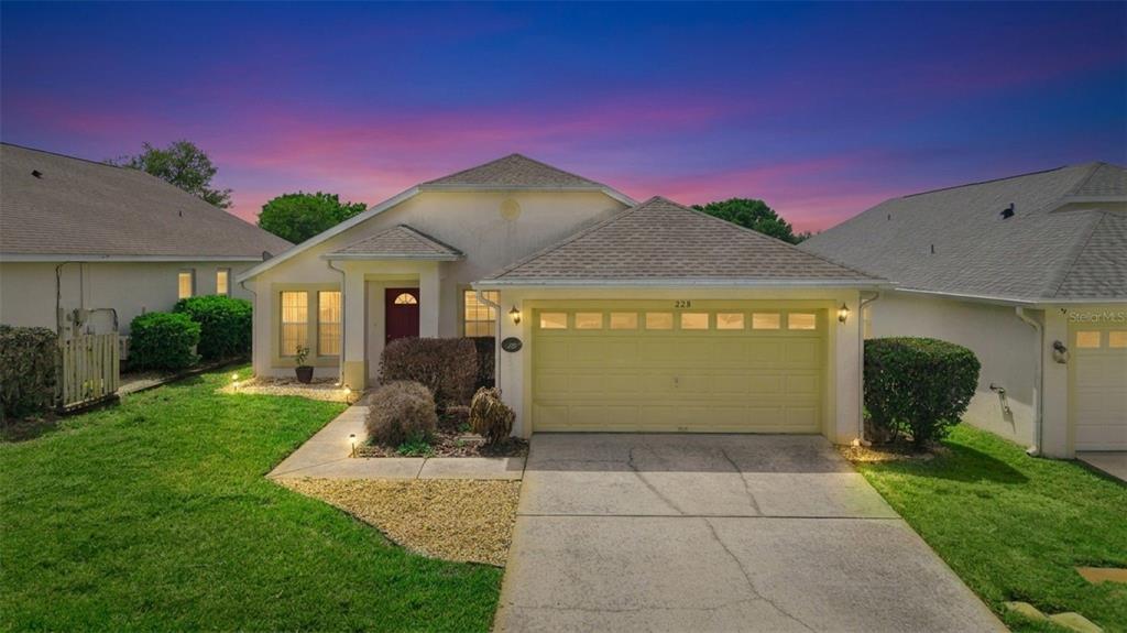 A single-story house with a beige stucco exterior, a two-car garage, and a front lawn — 228 TROON CIRCLE, DAVENPORT, FL