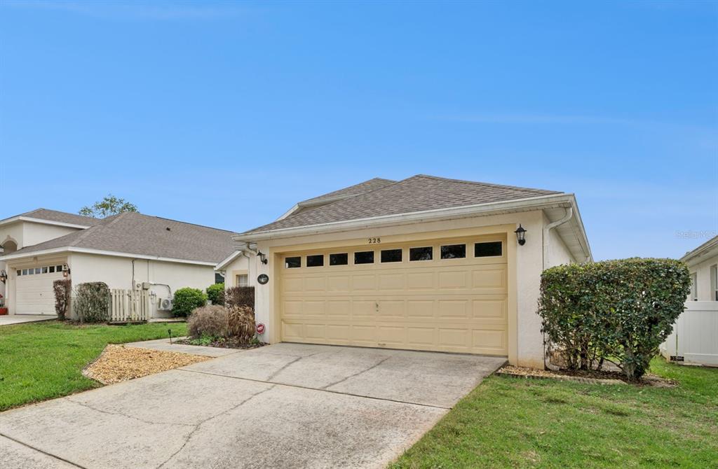 A beige house exterior features a two-car garage, a concrete driveway, and a manicured lawn — 228 TROON CIRCLE, DAVENPORT, FL