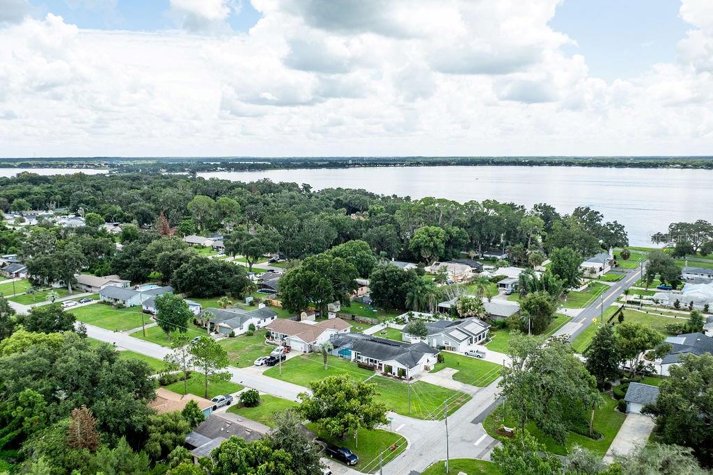 An aerial view shows a residential neighborhood with houses, green lawns, and a large lake — 4268 LAKE ELEANOR DRIVE, MOUNT DORA, FL