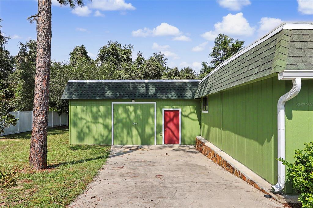 A green detached garage with a red door sits next to a green house exterior — 11840 N ANGUS HILLS TERRACE, DUNNELLON, FL