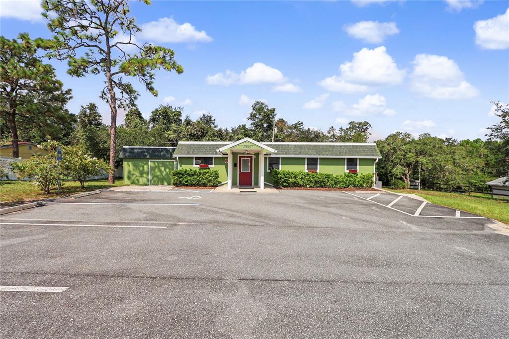 A single-story green building with a red front door sits behind a paved parking lot — 11840 N ANGUS HILLS TERRACE, DUNNELLON, FL