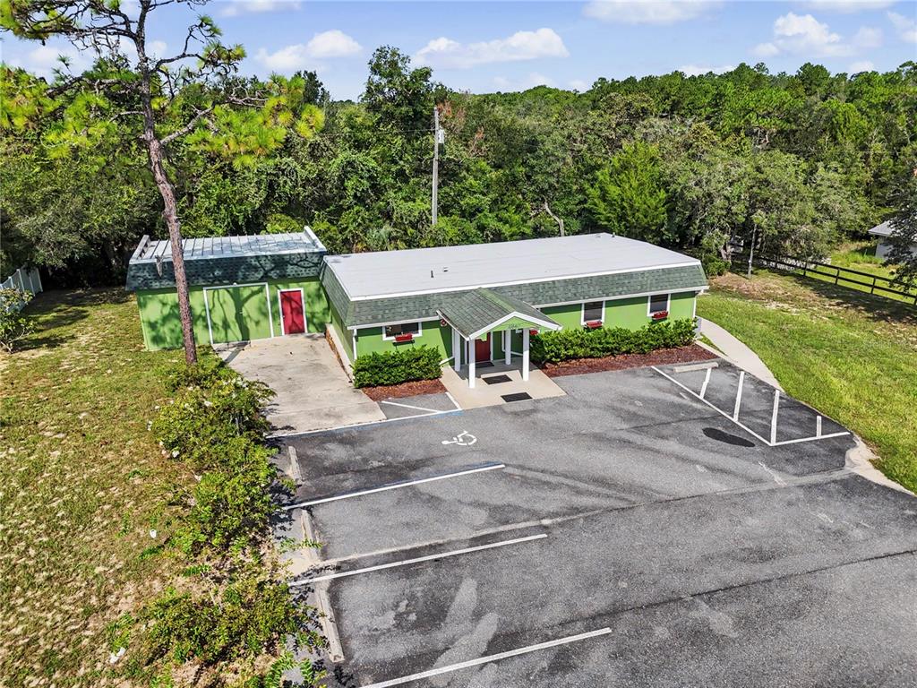 An aerial view of a green commercial building with a parking lot and surrounding trees — 11840 N ANGUS HILLS TERRACE, DUNNELLON, FL