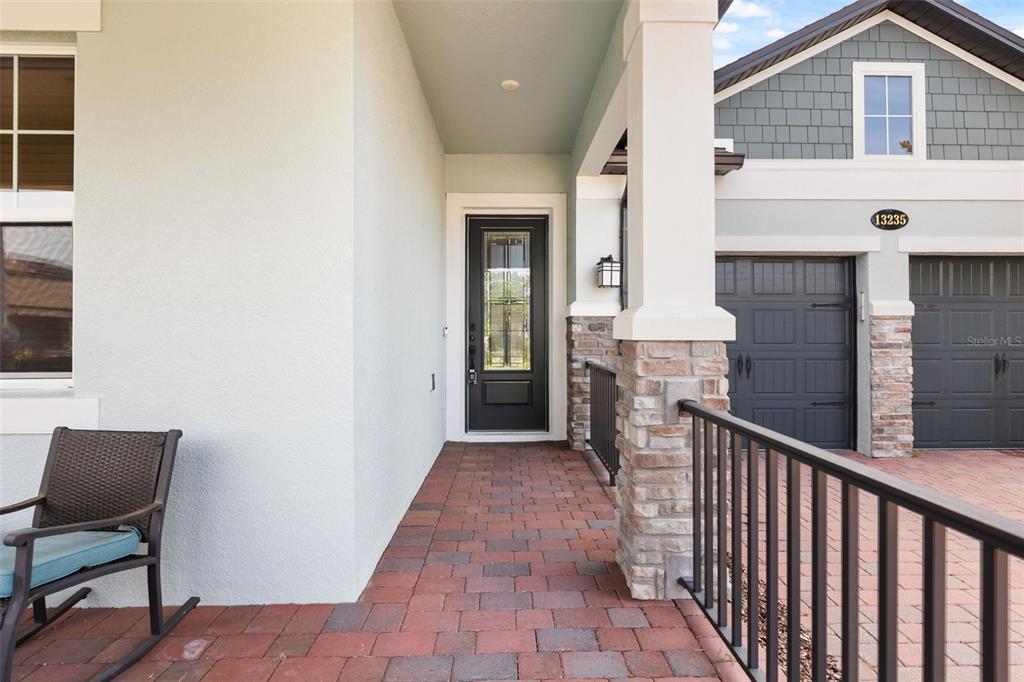 A covered brick porch leads to a dark front door beside a two-car garage — 13235 SPRING GROVE WAY, WINTER GARDEN, FL