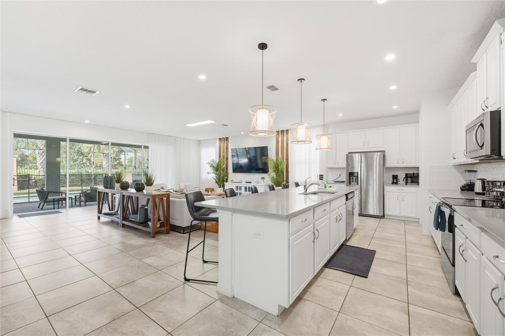 A bright open-concept kitchen and living area with white cabinets, a large island, and tile — 8967 AMELIA DOWNS TRAIL, KISSIMMEE, FL