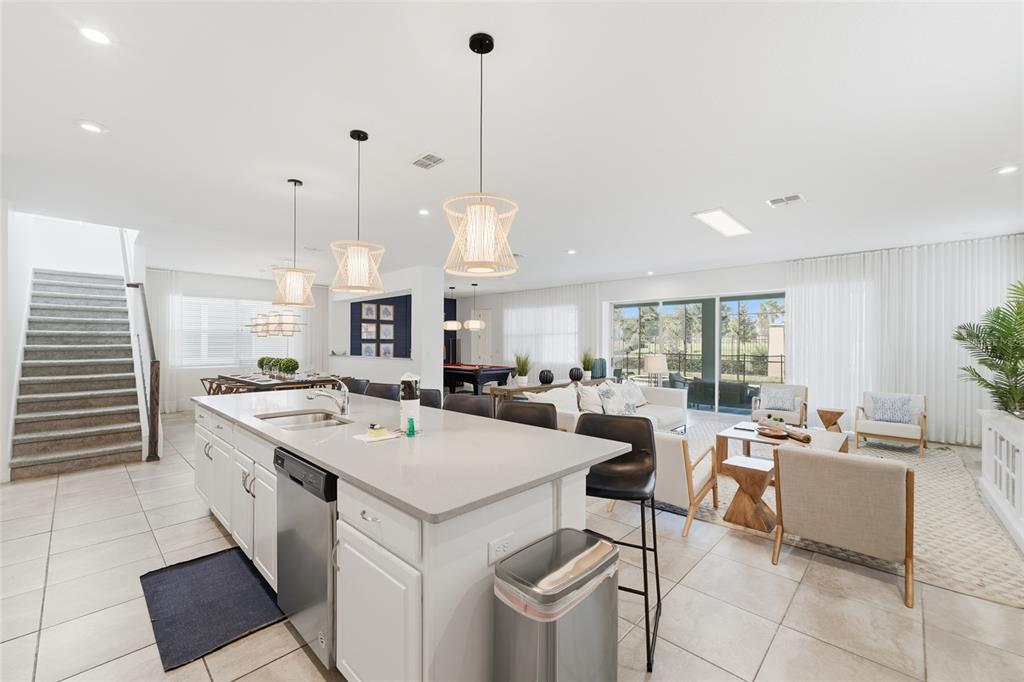 A bright, open-concept kitchen and living area features white cabinetry, pendant lighting, and tile floors — 8967 AMELIA DOWNS TRAIL, KISSIMMEE, FL