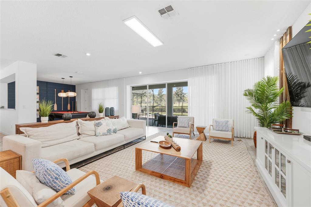 A bright living room features a large sectional sofa, wooden coffee table, and sliding glass doors — 8967 AMELIA DOWNS TRAIL, KISSIMMEE, FL