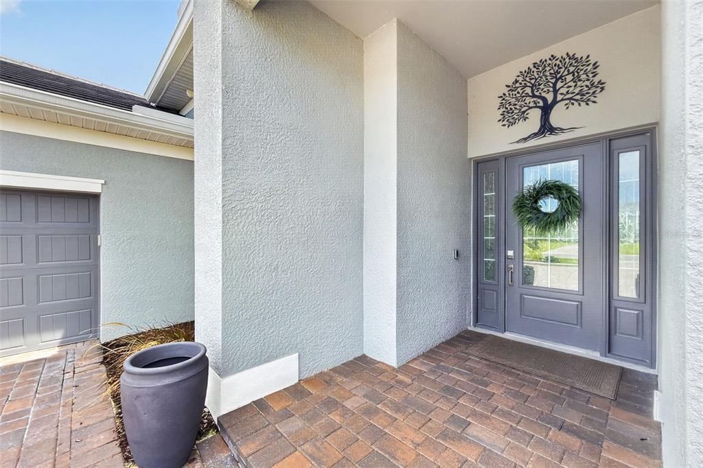 A gray front door with a wreath and tree wall art sits on a paved porch — 25076 REDWOOD COURT, PUNTA GORDA, FL