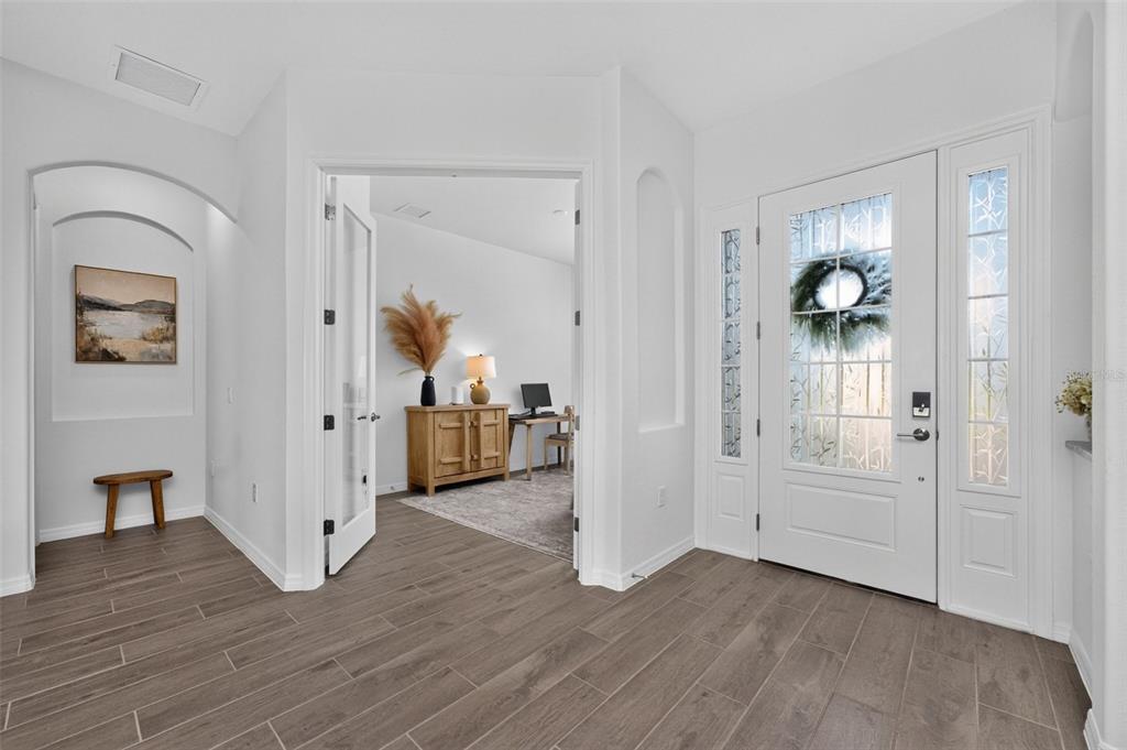 A bright entryway features wood-look tile flooring, a white front door, and a home office — 25076 REDWOOD COURT, PUNTA GORDA, FL