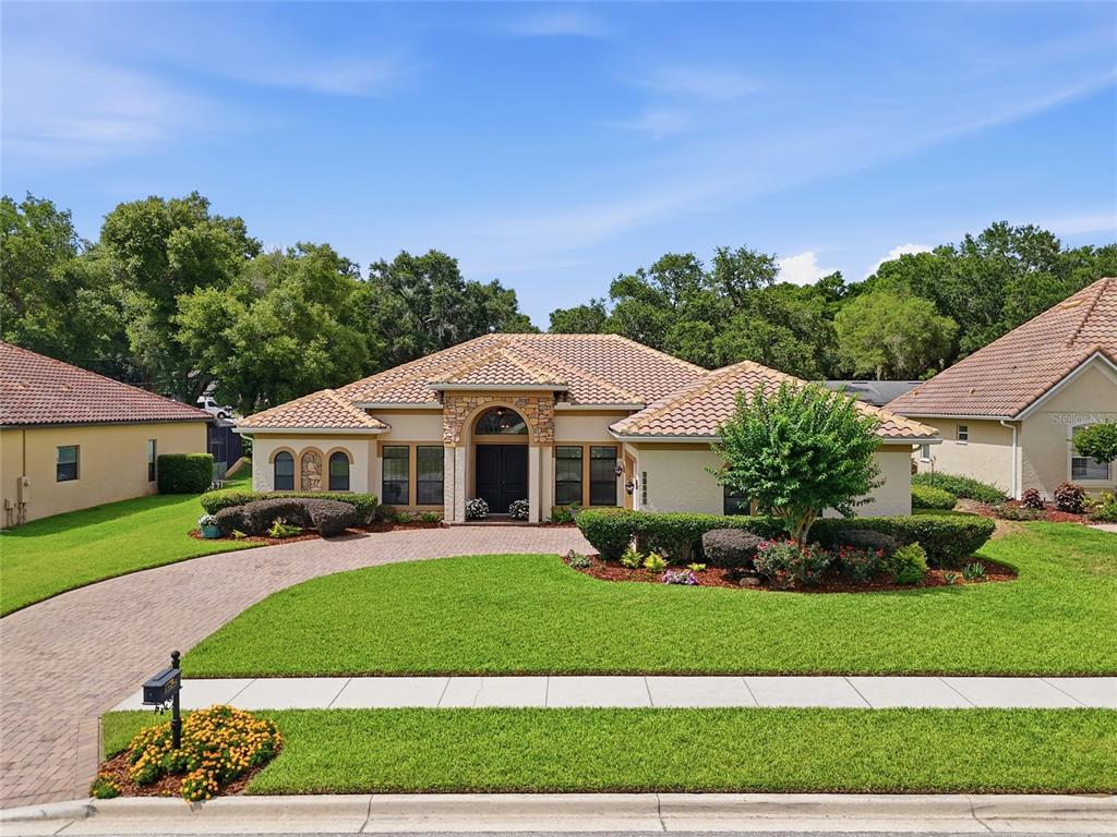 A single-story house with a tiled roof, stone entryway, and a brick driveway — 12825 BRUNELLO CIRCLE, CLERMONT, FL