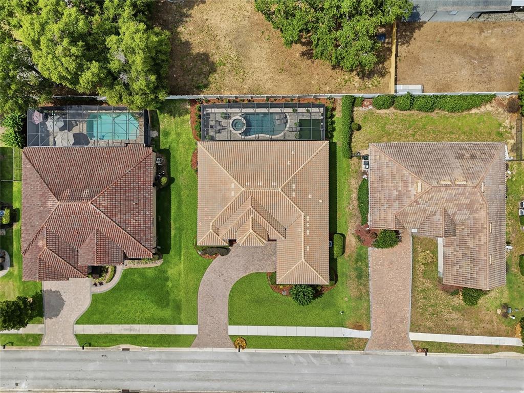 An aerial view shows three suburban houses with tiled roofs, driveways, and backyard swimming pools — 12825 BRUNELLO CIRCLE, CLERMONT, FL