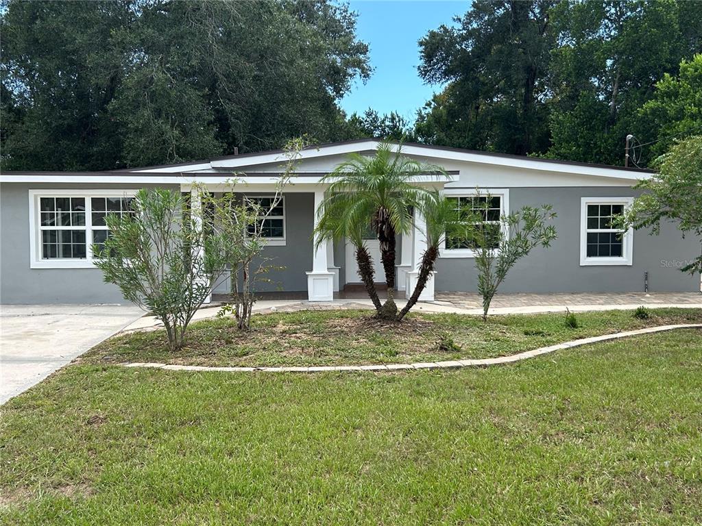 A single-story gray house features a covered front porch with white columns and a palm tree — 104 E GARDENIA DRIVE, ORANGE CITY, FL